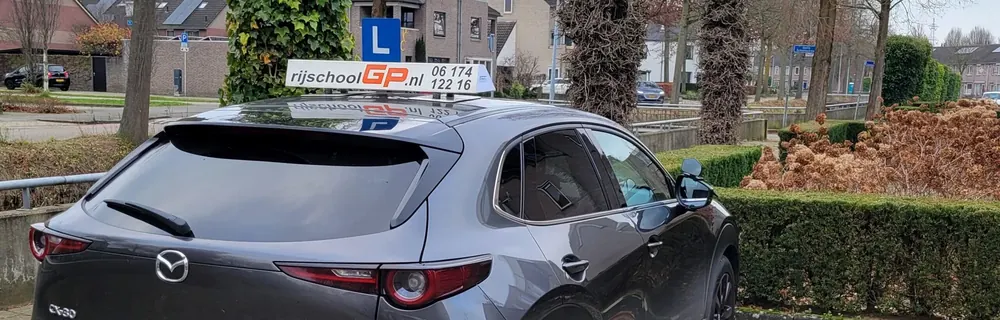 Grijze Mazda CX-30 van Rijschool GP met op het dak het daklicht met rijschoolGP.nl en 06 174 122 16